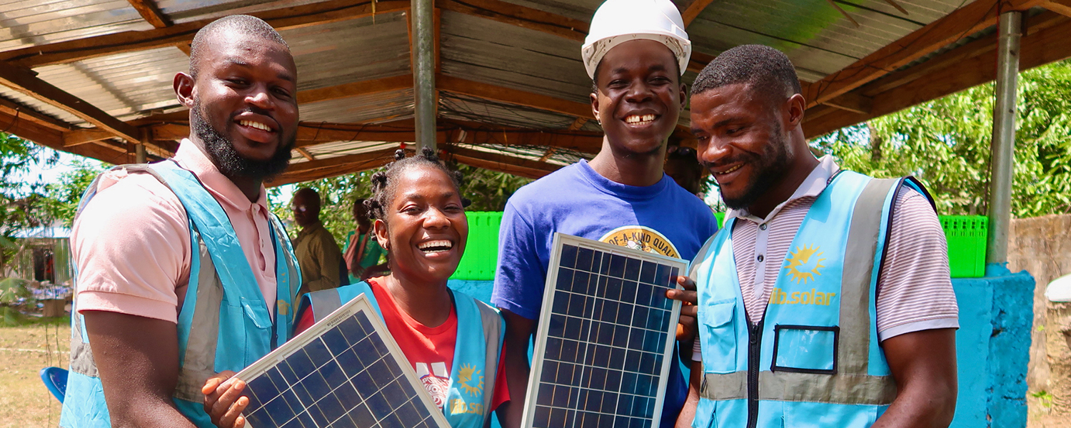 Group of Liberian men and women holding solar panels wearing vests labeled LIB Solar